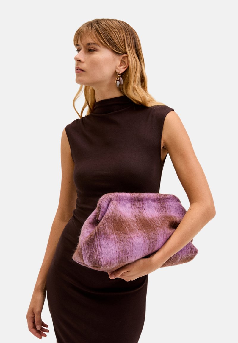 Borsa a tracolla in tessuto simile alla pelliccia nei colori viola e marrone, con una texture morbida, caratterizzata da un design pieghevole. Modello che tiene la borsa indossando un elegante abito scuro.