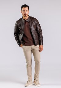 Brun läderjacka med kviltade axlar, vinröd stickad tröja under, beigefärgade slim-fit byxor och ljusbeiga sneakers.