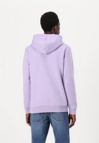 Light lavender hoodie with a soft texture, featuring a large hood and ribbed cuffs. Worn with blue denim jeans, viewed from the back.