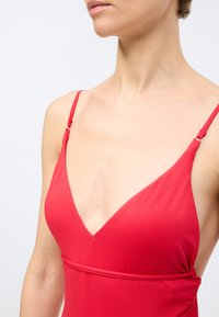 Γυναίκα που φοράει ένα αμάνικο κόκκινο φόρεμα με λεπτούς ρυθμιζόμενους ιμάντες και βαθύ ντεκολτέ σε σχήμα V, εμφανιζόμενη από τον λαιμό έως τη μέση.