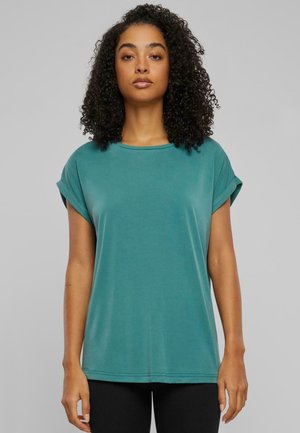 Teal kortärmad T-shirt med rund halsringning, mjuk textur och upprullade ärmar, som bärs med svarta leggings. Enkel och avslappnad design.