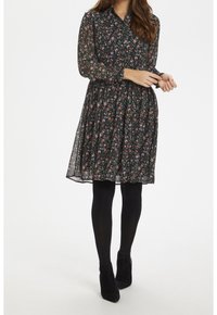 Czarna sukienka w kwiaty z długimi rękawami, kołnierzykiem, dopasowanym w talii i zwiewnym dołem. Połączona z czarnymi rajstopami i botkami na kostce.