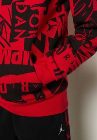 Punainen ja musta huppari graafisella printillä, jossa on ribbireunukset helmassa ja hihansuissa sekä kirjailtu logodetalji hihassa.