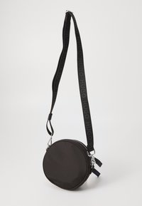 Czarna okrągła torba z zapięciem na zamek błyskawiczny, z płaskim paskiem z logo "HUGO" w kolorze czarnym, srebrnymi elementami metalowymi i teksturowanym wykończeniem.