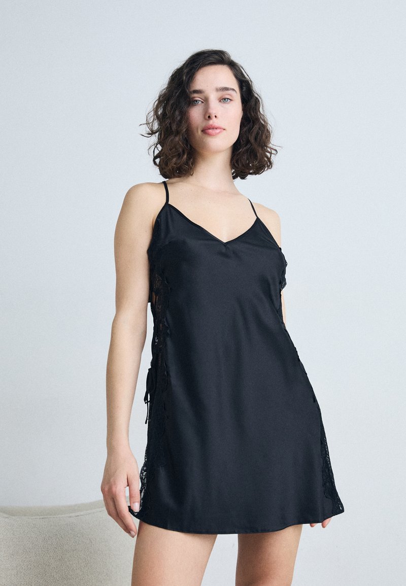 Black satin slip dress with thin straps, lace detailing on the sides, and a V-shaped neckline. Soft texture and relaxed fit.