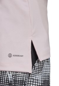 Haut de sport texturé rose clair avec fentes sur les côtés et logo AEROREADY noir. Associé à un legging noir et blanc à motifs.
