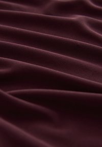 Tissu lisse, violet foncé, avec des plis doux et une texture subtile créant de douces ondulations à la surface.