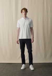 Witte poloshirt met korte mouwen, gecombineerd met een donkere broek en witte sneakers. Het shirt heeft een klassieke kraag en een aansluitende pasvorm.