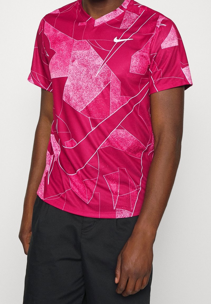 Czerwona sportowa koszulka z geometrycznym wzorem oraz nieregularnymi białymi akcentami, krótkimi rękawami i okrągłym dekoltem. Logo Nike na piersi.