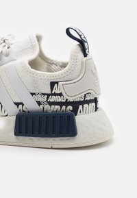 Vit atletisk sneakers med en strukturerad stickad ovandel, blå detaljer och en distinkt randig design på sulan med logotypdetaljer.