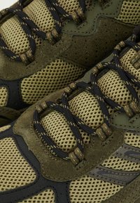 Olíva zöld sportcipők, hálós és velúrból készült felsőrésszel, fekete kiegészítőkkel és texturált fűzőkkel, lélegző kialakítással és párnázott talppal.