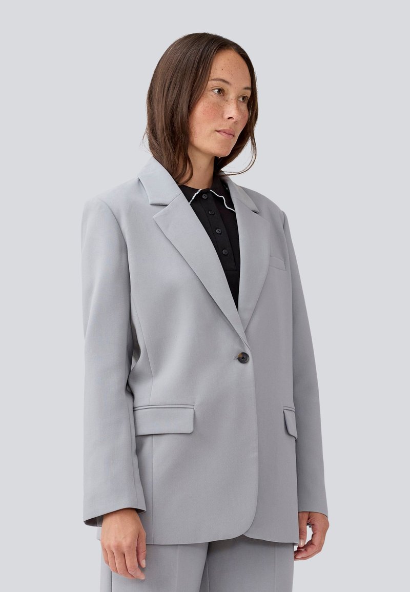 Light gray blazer made of fabric with a smooth texture, featuring a single button closure, notched lapels, and front pockets.