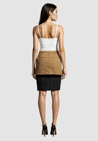 Falda de lápiz a rayas marrón y negra con bolsillos traseros, que presenta un diseño ajustado y una textura suave. Llevada con una camiseta sin mangas blanca y tacones.