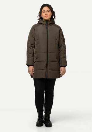 Manteau long en khaki rembourré avec capuche, fermeture éclair à l'avant et poches latérales. Tissu texturé avec un motif matelassé. Pantalons noirs et bottes complètent le look.
