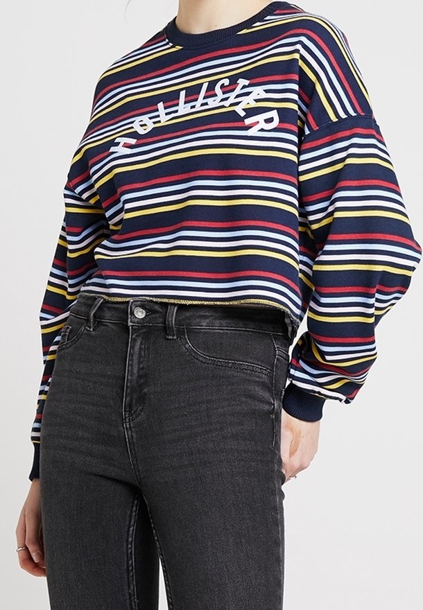 Marinblårandig tröja med röda, gula och vita horisontella ränder; har en cirkulär logotyp "Hollister" i vitt över bröstet.