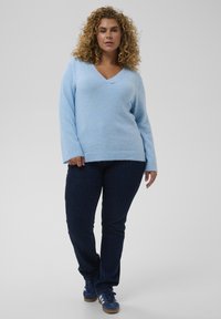 Pull léger bleu clair à col en V en tricot doux et texturé ; associé à un jean denim bleu foncé et des baskets bleu marine. Coupe décontractée avec manches longues.