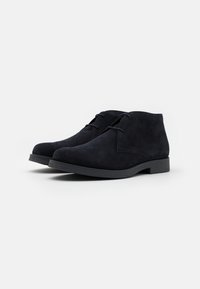 Bottines chukka en suede noir avec un bout rond, une fermeture à lacets et une semelle en caoutchouc texturé. Fini lisse et détails de couture minimaux.