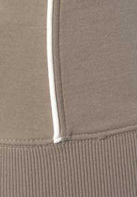 Hellbrauner Stoff mit einer gerippten Textur. Eine kontrastierende weiße Naht verläuft vertikal entlang der glatten Oberfläche und betont die Linien des Designs.