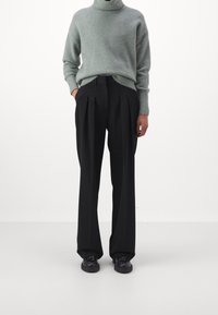 Hellgrüner, grob gestrickter Rollkragenpullover mit lockerer Passform, kombiniert mit hoch taillierten, schwarzen, plissierten Hosen und schwarzen Schuhen.