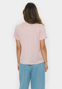 Roza majica s kratkimi rokavi, nekoliko sijoče teksture, ravnega kroja in okroglega ovratnika; v kombinaciji s svetlo modrimi širokimi hlačami.