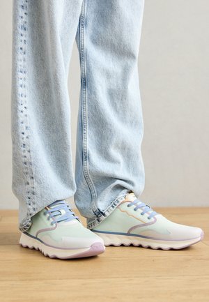 Pastelgroene en witte sneakers met paarse accenten, textielstof en een golvende, gevoerde zool; gecombineerd met lichtblauwe spijkerbroek.
