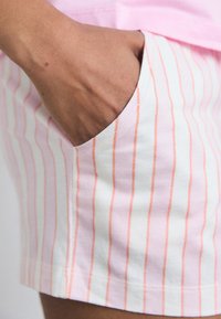 Calções de algodão com uma base branca e finas riscas verticais em rosa e laranja, com um bolso lateral e um corte descontraído.