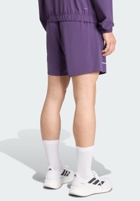 Lila Sportkurze aus leichtem Stoff, mit einem elastischen Bund und reflektierenden Akzenten. Kombiniert mit weißen Socken und Schuhen.