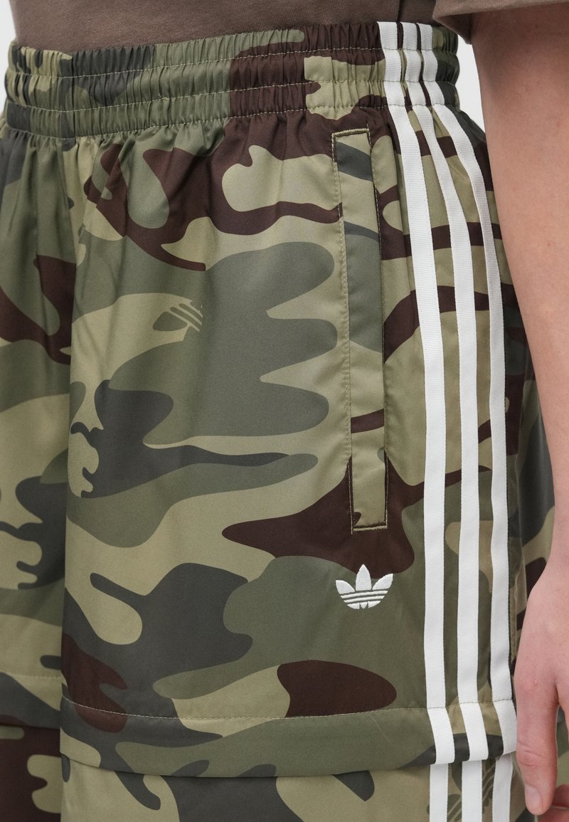 Tarnshorts in Grüntönen und Braun, mit elastischem Bund, seitlichen Taschen und drei weißen Streifen an den Seiten.