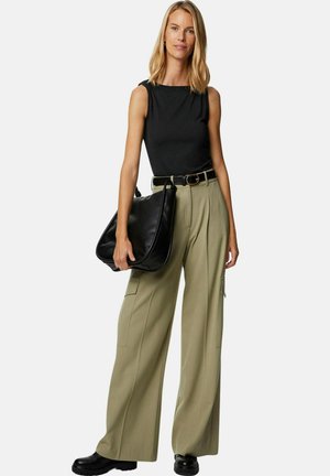 Top senza maniche nero, pantaloni larghi verde oliva con tasche cargo, cintura nera e grande borsa nera a spalla; modella con scarpe nere chunky.