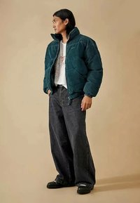 Τελαρίνης πανωφόρι σε τιρκουάζ απόχρωση με ψηλό γιακά, φερμουάρ στην μπροστινή πλευρά και πλαινές τσέπες, συνδυασμένο με φαρδιά τζιν σε σκούρο χρώμα και μαύρα υποδήματα.