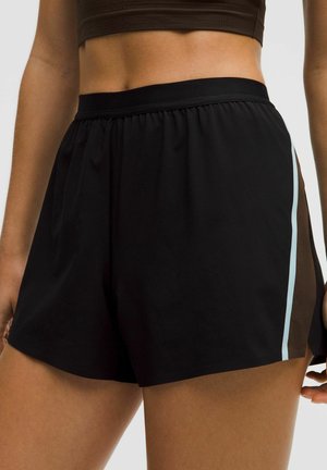 Zbliżenie osoby noszącej czarne sportowe szorty z jasnoniebieskim paskiem po boku oraz ciemny krótki top odsłaniający brzuch i górną część ud.