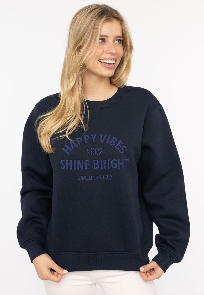 Dunkelblaues Sweatshirt mit Rundhalsausschnitt und langen Ärmeln. Mit gesticktem Text "HAPPY VIBES" und "SHINE BRIGHT" in kontrastierenden Farben.