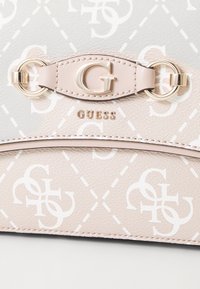 Borsa sintetica rosa chiaro con logo "G" in rilievo, motivo geometrico, dettagli in metallo dorato e il nome del brand "GUESS" esposto.