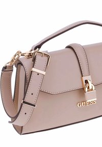 Borsa a tracolla in finta pelle beige con accessori dorati, forma rettangolare, tracolla regolabile e marchio "GUESS" impresso sul davanti.