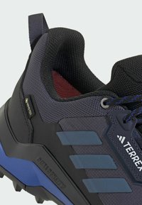 Čierna a tmavosivá turistická obuv s priedušnou látkou, označením Gore-Tex, modrými akcentmi a robustným dizajnom podrážky. Obsahuje odolné materiály a textúrovaný povrch.