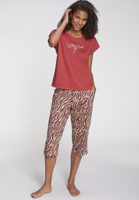 Červené bavlnené tričko s grafikou "Divoký v srdci". Lichotivé capri nohavice majú viacfarebný vlnitý vzor a voľný strih.