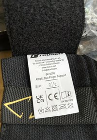 Schwarze Fingerstütze mit strukturiertem Stoff und verstärkten Kanten. Enthält ein Etikett mit Größe (8½) und Pflegehinweisen. Goldene Akzente sind ebenfalls enthalten.