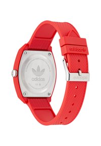 Punane silikoonist rihmaga kell, millel on roostevabast terasest tagakülg, kuusnurkne korpus, tekstuuriga rihm ja Adidas logo klambri peal.