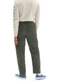 Pantalones cargo verdes de corte relajado, con bolsillos traseros y laterales, combinados con una camisa de manga larga color crema y zapatillas azules.