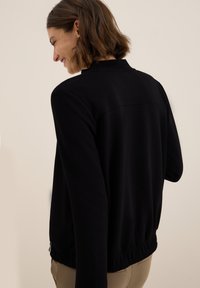 Sweatshirt noir avec coupe décontractée, ourlet élastiqué et texture douce. Design simple avec col montant et épaules tombantes.