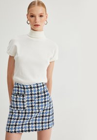 Witte geribbelde turtleneck met korte mouwen, gecombineerd met een blauw en zwart geruit minirok met voorzakken en een gestructureerd patroon.