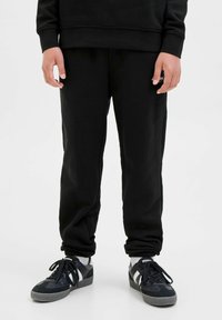 Svarta träningsbyxor i mjukt tyg med avslappnad passform, med elastiska muddar och sidofickor, kombinerat med svarta sneakers.