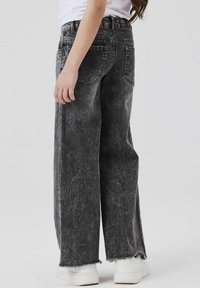 Vaqueros de mezclilla gris con un corte holgado, dobladillos deshilachados y diseño de cinco bolsillos, combinados con zapatillas blancas.