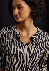 Zwarte en beige blouse met een zebraprint, een V-hals en driekwart mouwen van een gladde, lichte stof.