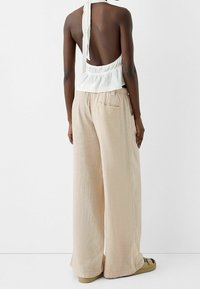 Witte, textuurvolle top zonder rug met een halterstrik, gecombineerd met losse, lichtbeige broek met zakken en een relaxte pasvorm.