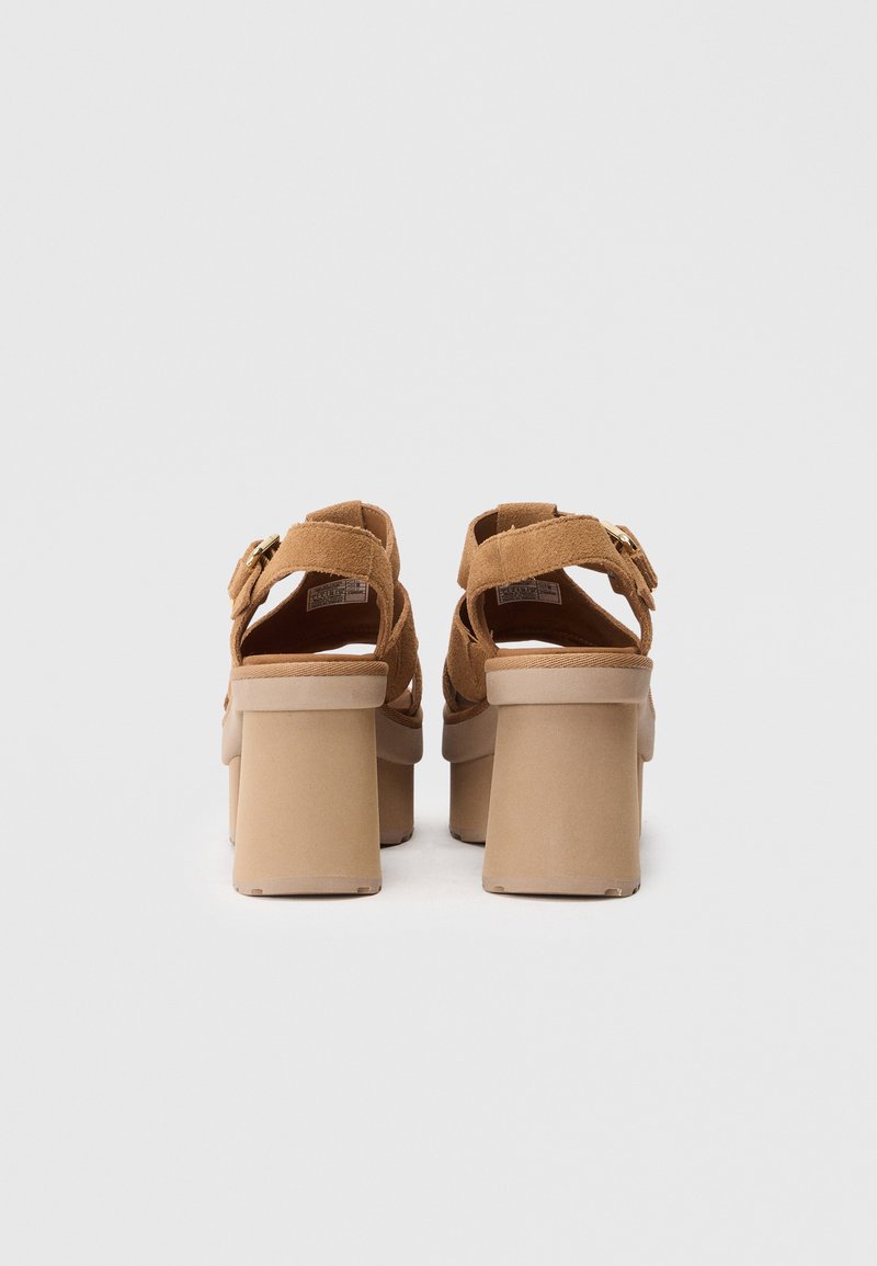 Sandalias de plataforma de ante marrón con un tacón grueso, espalda abierta y correa ajustable con un hebilla dorada.