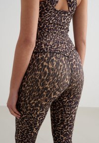 Leopardmønstret jumpsuit med en tettsittende design, som har en mørk brun og beige fargekombinasjon, teksturert stoff og en utskjæring på ryggen.
