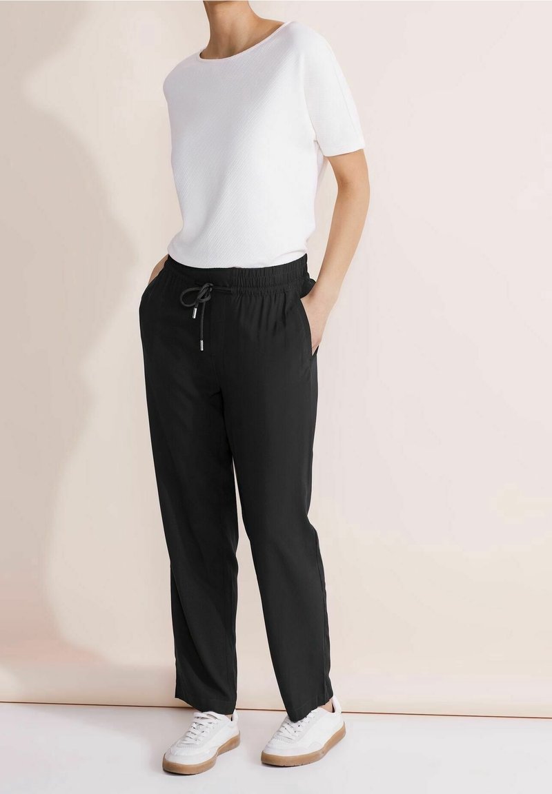 Chemise blanche à manches courtes avec texture côtelée, associée à un pantalon noir à taille élastique et des baskets blanches avec des semelles marron.