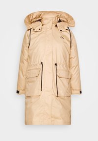 Beige waterproof parka with a high collar, adjustable hood, front zip, two patch pockets, and brown accent details.