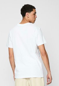 Hvid bomulds T-shirt med korte ærmer, rund hals og en ensfarvet bagdesign. Glat tekstur, afslappet pasform, minimal dekoration.